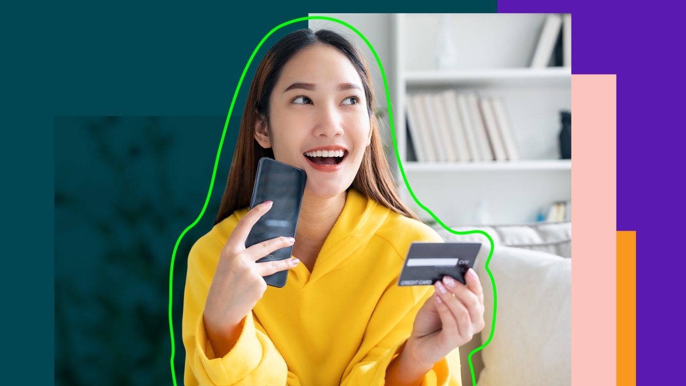 Smiling Asian woman, holding a bank card and a smartphone