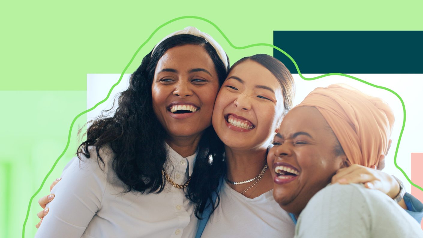 Three women hugging and smiling on a green background.