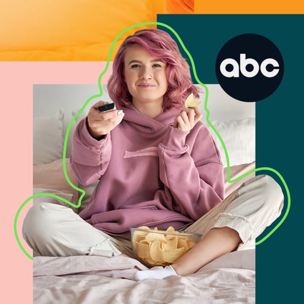 Young woman with pink hair and a bowl of crisps, using a remote control