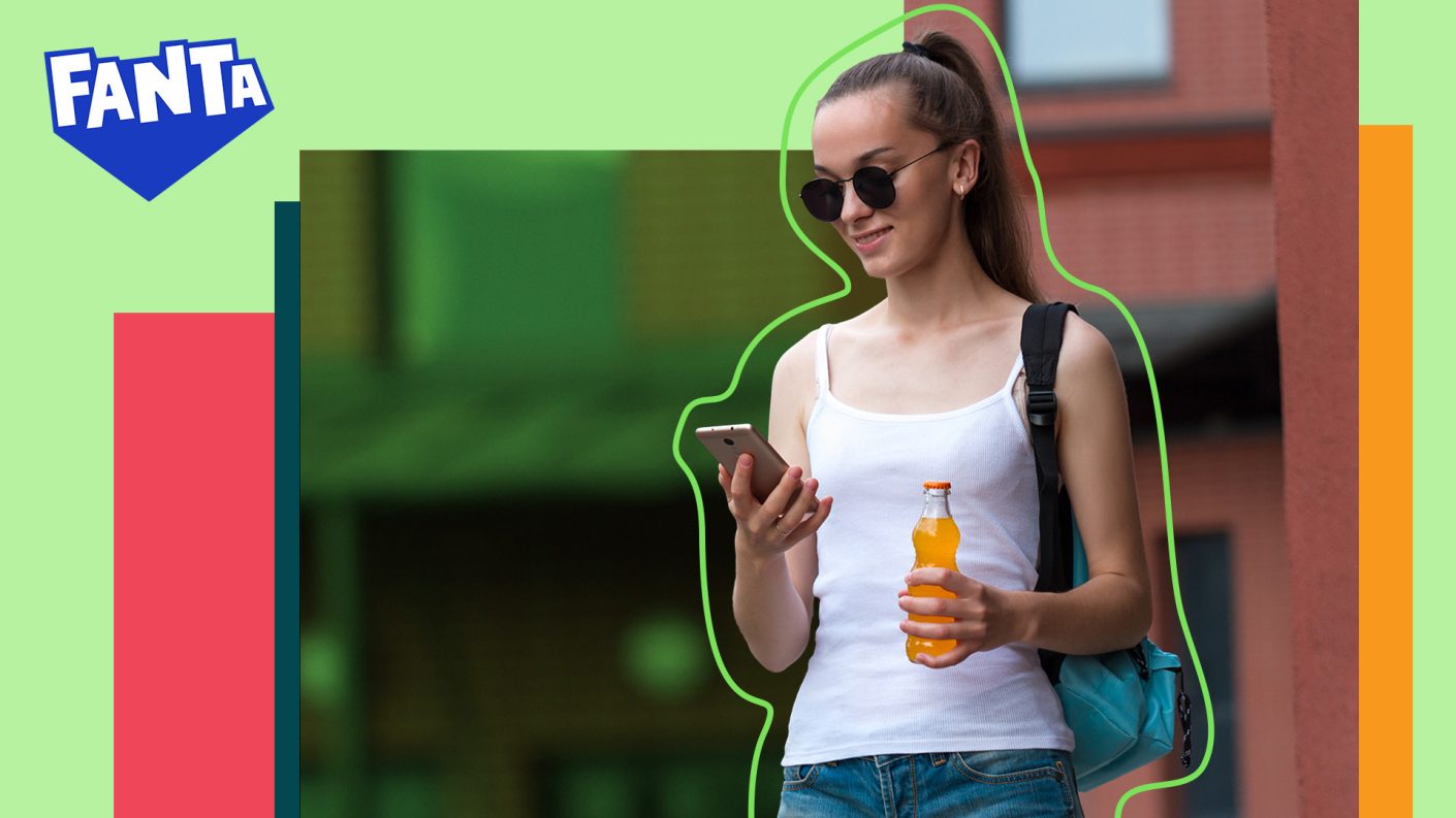 A person looking at their phone holding a Fanta bottle
