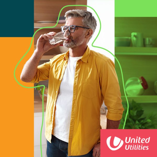 Man with grey hair and beard, wearing glasses and yellow shirt drinking water