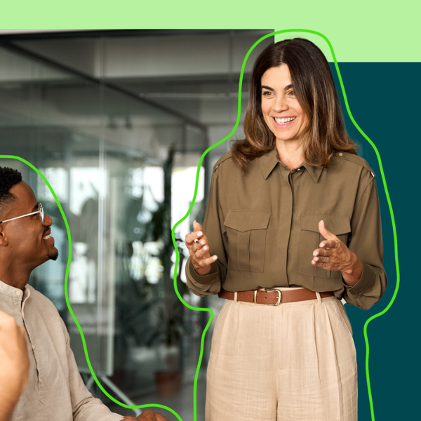 Person in a meeting standing up, smiling and presenting to two other people in the room.