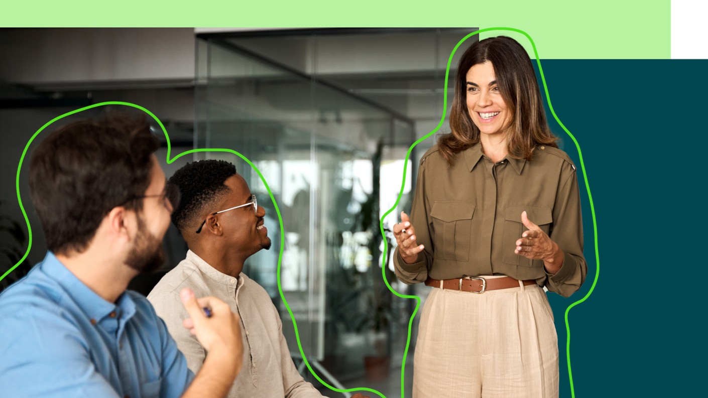 Person in a meeting standing up, smiling and presenting to two other people in the room.